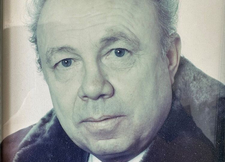 Porträt eines älteren Mannes mit kurzem, lockigem Haar, der einen Mantel mit Pelzkragen und Krawatte trägt.