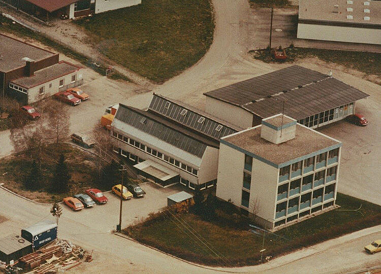 Luftaufnahme eines Industriegebiets mit mehreren Gebäuden, Parkplätzen und mehreren geparkten Autos auf unbefestigten Straßen.